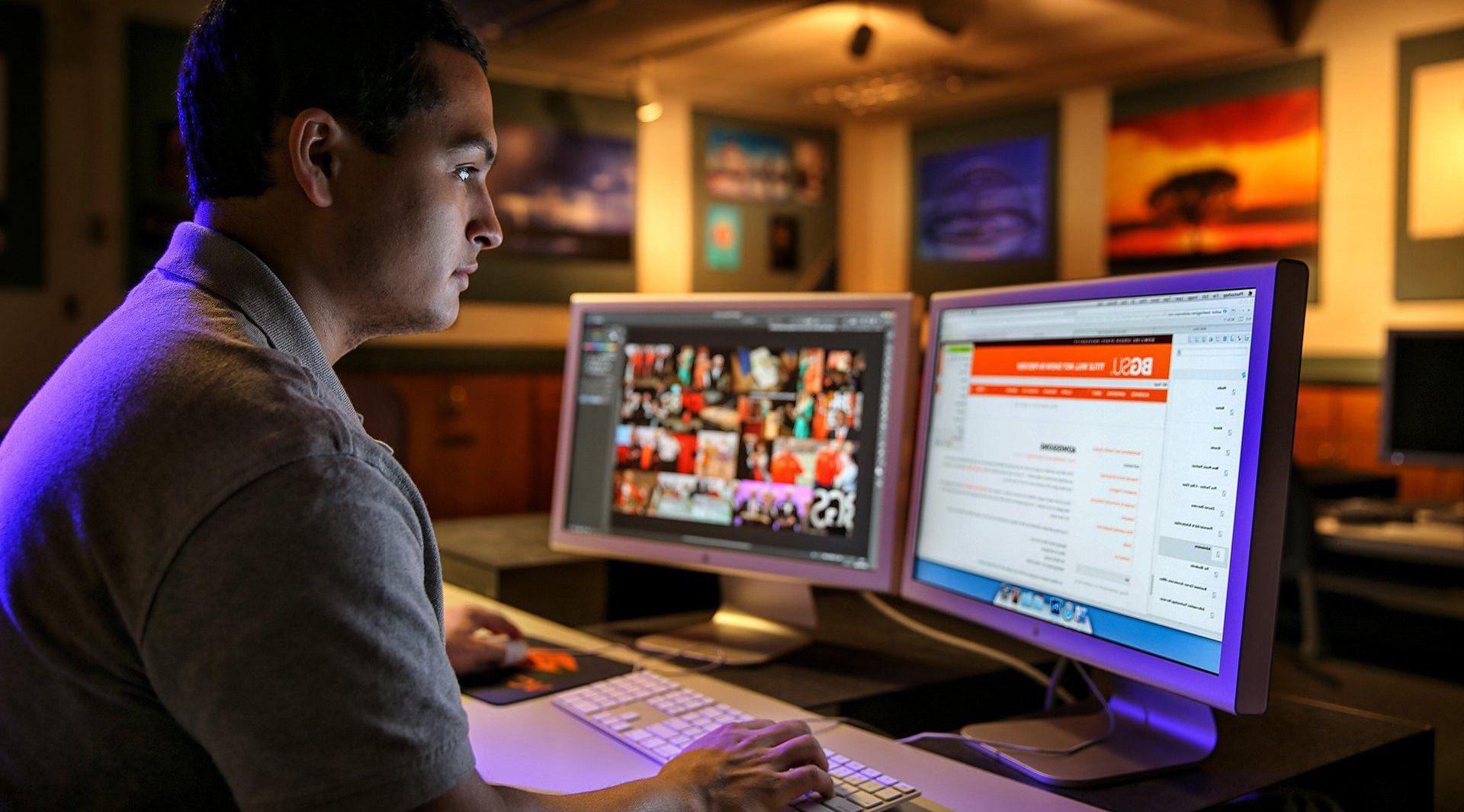 A male VCT student at BGSU sits in front of two computer monitors 和 works on the BGSU website.